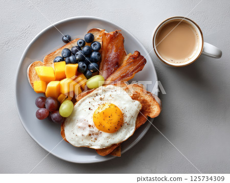Breakfast toast with fried egg, bacon, fresh fruit, and coffee on gray plate, colorful and appetizing morning meal 125734309