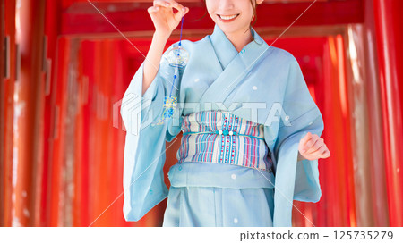 日本的夏天：一位穿著浴衣的女子站在鳥居門前，手裡拿著風鈴 125735279
