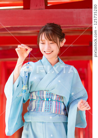 日本的夏天：一位穿著浴衣的女子站在鳥居門前，手裡拿著風鈴 125735280