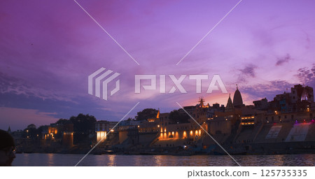 Varanasi, Uttar Pradesh, India. People walking on steps near Sri Suparshwanath Bhagwaan Jain Digamber Mandir temple neat Jain Ghat. Evening pink purple sunset sky, night time. Camera moving along Varanasi, Uttar Pradesh, India. People walking on steps near Sri Suparshwanath Bhagwaan Jain Digamber Mandir temple neat Jain Ghat. Evening pink purple sunset sky, night time. Camera moving along 125735335