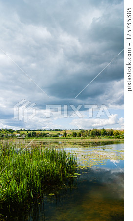 Rural landscape, rain clouds over the pond, vertical photo Rural landscape, rain clouds over the pond, vertical photo 125735385