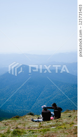 Two people sitting on top of a mountain and looking at the landscape in summer 125735403