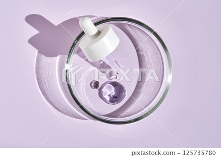 A pipette with a drop of serum in a petri dish on a purple background. 125735780