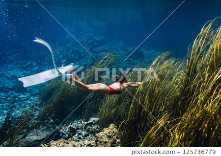 Woman dives underwater in transparent lake with algae. Freediving in crystal blue lake Woman dives underwater in transparent lake with algae. Freediving in crystal blue lake 125736779