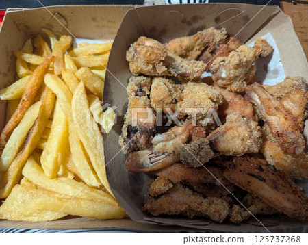 Traditional breaded chicken legs and French fries in a cardboard delivery box Traditional breaded chicken legs and French fries in a cardboard delivery box 125737268