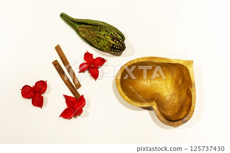 Heartshaped bowl with red flowers and cinnamon sticks around it Heartshaped bowl with red flowers and cinnamon sticks around it 125737430