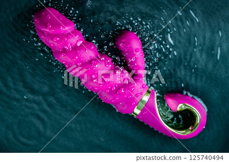 Pink ribbed vibrator in water. Circles on water around sex toy. Pink ribbed vibrator in water. Circles on water around sex toy. 125740494