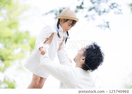 特寫:一對父女在公園裡高高地抱著女兒,背景是藍天,展現他們的幸福、未來和幸福 特寫:一對父女在公園裡高高地抱著女兒,背景是藍天,展現他們的幸福、未來和幸福 125740968