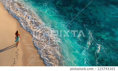 A woman walking along the shoreline and the emerald blue sea 125743101