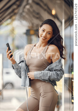 Woman in a summer city. Lady with phone. Brunette by the building. 125743529