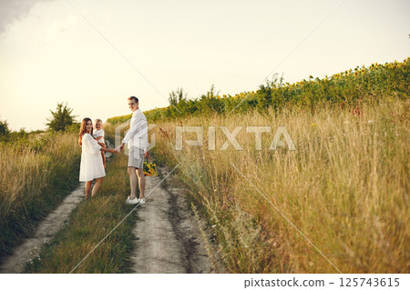 Photo of a young family walking at the field on a sunny day. Brunette mother, father and their little blonde son posing for a photo. Mother holding her son on a hands. Photo of a young family walking at the field on a sunny day. Brunette mother, father and their little blonde son posing for a photo. Mother holding her son on a hands. 125743615