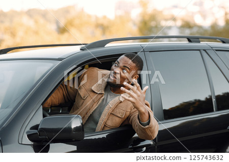 Closeup portrait of nervous young black man sitting in his car. Man with beard wearing brown jacket. Male driver looking nervous. 125743632
