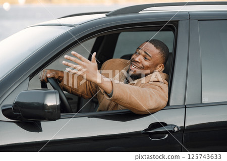 Closeup portrait of nervous young black man sitting in his car. Man with beard wearing brown jacket. Male driver looking nervous. 125743633