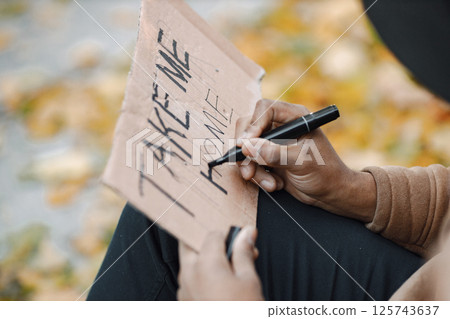 Focus on a cardboard sign. Young black man hitchhiking on road and holding a sign take me home. Male traveler traveling alone by autostop. 125743637