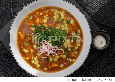 Traditional Russian cold soup okroshka combining kvass, diced potatoes, cucumbers, radishes, garnished with fresh herbs and creamy sour cream dollop Traditional Russian cold soup okroshka combining kvass, diced potatoes, cucumbers, radishes, garnished with fresh herbs and creamy sour cream dollop 125743934