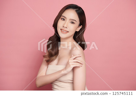 A beautiful young Asian woman with clean, fresh skin against a pink background. Skincare, facial treatment, cosmetology, beauty, and spa. An elegant portrait of an Asian woman. 125745111