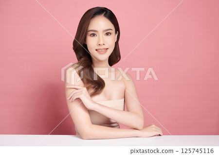 A beautiful young Asian woman with clean, fresh skin against a pink background. Skincare, facial treatment, cosmetology, beauty, and spa. An elegant portrait of an Asian woman. A beautiful young Asian woman with clean, fresh skin against a pink background. Skincare, facial treatment, cosmetology, beauty, and spa. An elegant portrait of an Asian woman. 125745116