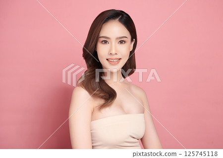 A beautiful young Asian woman with clean, fresh skin against a pink background. Skincare, facial treatment, cosmetology, beauty, and spa. An elegant portrait of an Asian woman. A beautiful young Asian woman with clean, fresh skin against a pink background. Skincare, facial treatment, cosmetology, beauty, and spa. An elegant portrait of an Asian woman. 125745118