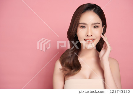 A beautiful young Asian woman with clean, fresh skin against a pink background. Skincare, facial treatment, cosmetology, beauty, and spa. An elegant portrait of an Asian woman. A beautiful young Asian woman with clean, fresh skin against a pink background. Skincare, facial treatment, cosmetology, beauty, and spa. An elegant portrait of an Asian woman. 125745120