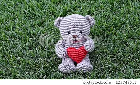 Adorable Crochet Teddy Bear Holding a Red Heart on Green Grass 125745515