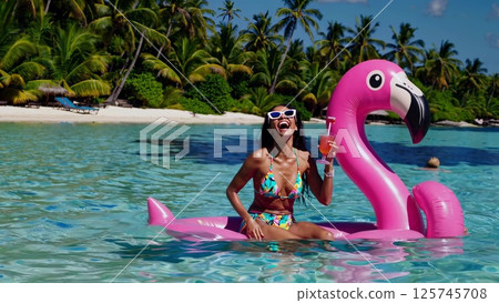 Tourist enjoying a cocktail on a giant inflatable flamingo Tourist enjoying a cocktail on a giant inflatable flamingo 125745708