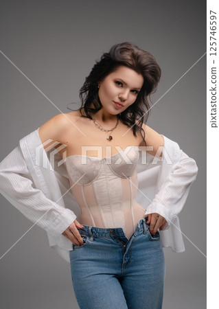 Elegant woman showcases fashionable corset and casual jeans in stylish pose Elegant woman showcases fashionable corset and casual jeans in stylish pose 125746597
