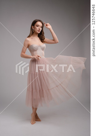 Elegant woman in corset and flowing skirt poses in a soft fashion shoot 125746648
