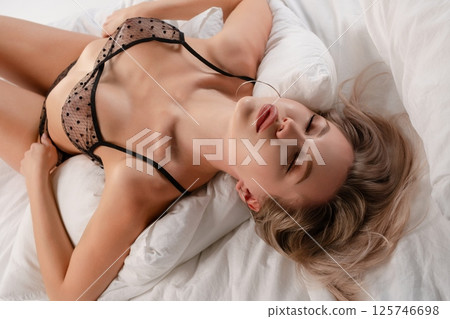 Elegant woman in stylish lingerie resting on soft pillows in a serene setting 125746698