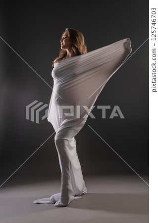 Pregnant woman elegantly posing in white fabric with a beautiful silhouette 125746703
