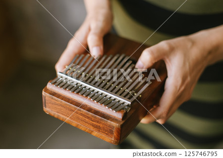 Close-up of hands holding a wooden kalimba musical instrument. Close-up of hands holding a wooden kalimba musical instrument. 125746795