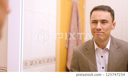 Businessman smiling at himself in bathroom mirror Businessman smiling at himself in bathroom mirror 125747234