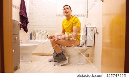 Man sitting on toilet finishing toilet paper roll and yelling Man sitting on toilet finishing toilet paper roll and yelling 125747235