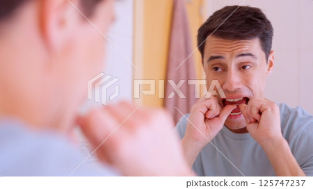 Man flossing teeth in bathroom mirror, oral hygiene routine Man flossing teeth in bathroom mirror, oral hygiene routine 125747237