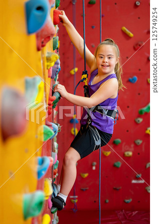 Child Climbing Indoor Rock Wall in Gym With Colorful Holds and Safety Gear 125749254
