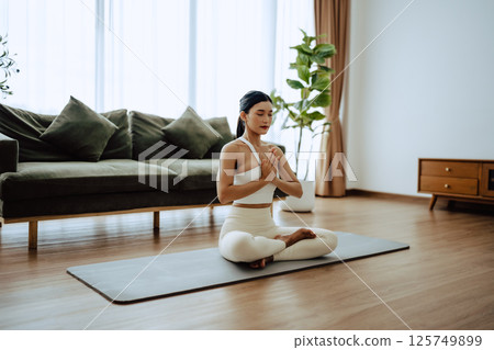 Young Asian woman meditating in lotus position at home 125749899