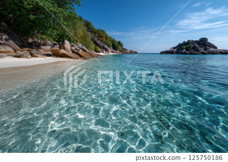Crystal clear water gently laps against rocky beach, surrounded by lush trees under bright blue sky. serene landscape invites relaxation and tranquility 125750186