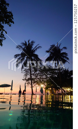 Tourists enjoying sunset at infinity pool overlooking tropical ocean 125750257