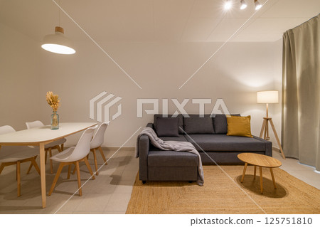 Living room view with grey sectional sofa and round coffee table next to the dining area in a cozy apartment 125751810