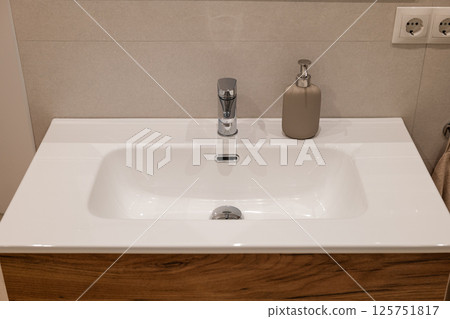 Top view of bathroom sink with chrome faucet, beige soap dispenser and wooden vanity base 125751817