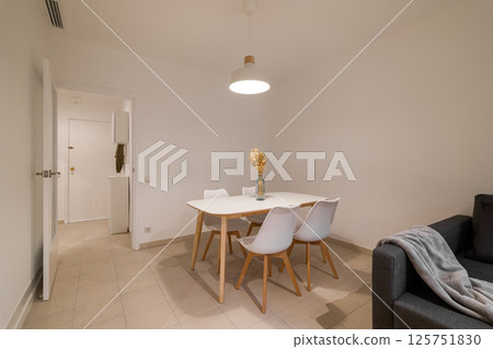 Compact dining zone with a white table and four matching chairs set beside a dark sofa in the living space 125751830