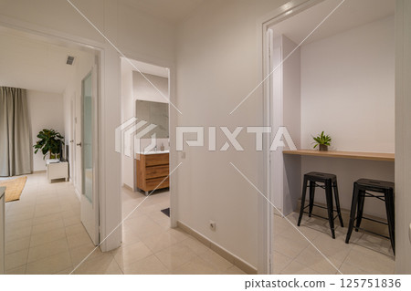 Hallway with beige tiled floor, white walls and entry to kitchen area with bar stools Hallway with beige tiled floor, white walls and entry to kitchen area with bar stools 125751836