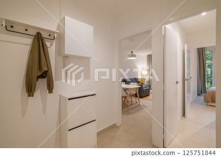 Bright hallway with white walls, beige tiled floor and open doorways leading to living and bedroom 125751844