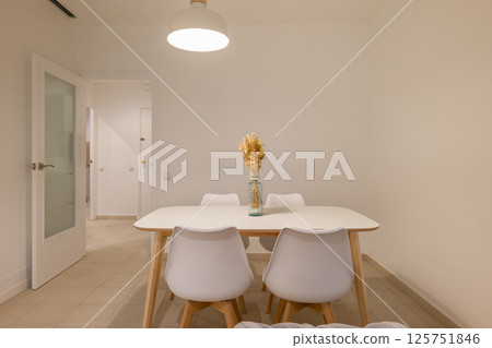 Dining area with vase centerpiece on a white table and four chairs near the apartment entrance Dining area with vase centerpiece on a white table and four chairs near the apartment entrance 125751846