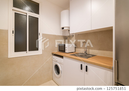 Compact kitchen sink area with wood countertop, white cabinets, stainless steel faucet and microwave 125751851