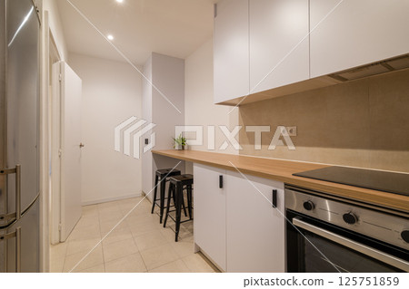 Modern kitchen perspective with bar counter, stools, white cabinetry and wood countertop finish 125751859