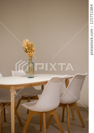 Dining area with white chairs, wood trim table and dried flowers in blue glass vase centerpiece 125751864