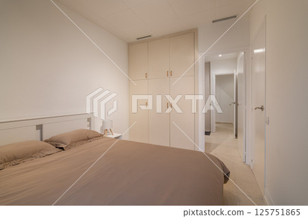 Spacious bedroom with taupe bedding, white built-in wardrobe and doorways to hallway Spacious bedroom with taupe bedding, white built-in wardrobe and doorways to hallway 125751865