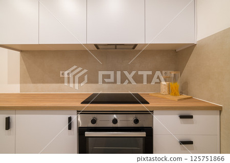 Kitchen stove area with glass cooktop, white cabinetry, wood counter and clean backsplash wall 125751866