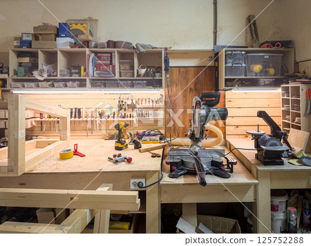 Carpentry workshop with power tools, wood planks, tape, industrial equipment, and organized workspace on a sturdy bench 125752288