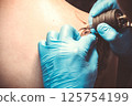 Artist in Blue Gloves Tattooing on the Back 125754199